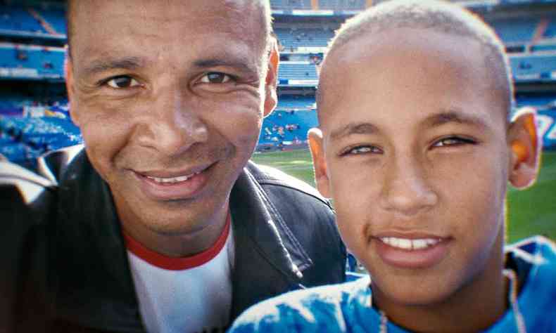 Foto antiga mostra Neymar pai e Neymar Jr, ainda garoto, sorrindo, tendo ao fundo um campo de futebol