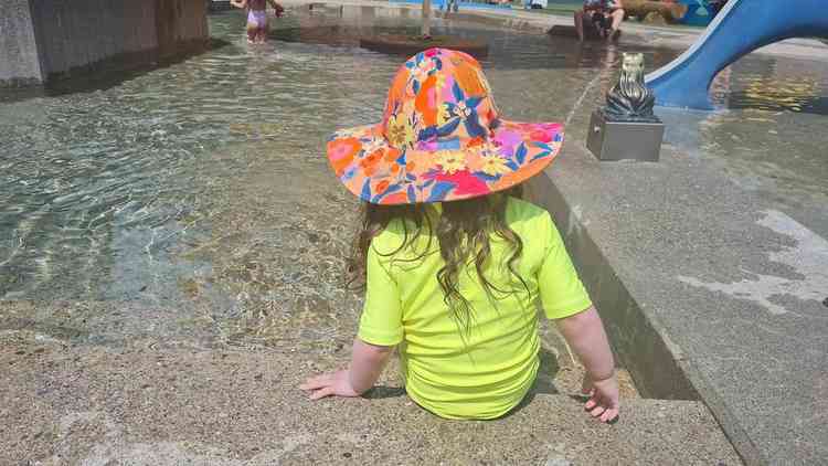 Criana com roupa de banho amarelo neon e chapu,  beira de uma piscina 