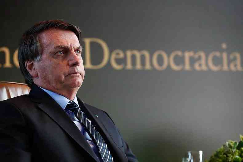 Jair Bolsonaro perfil; ao fundo um painel com a palavra democracia 