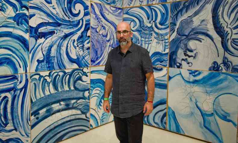 O escritor Valter Hugo Mãe está em Inhotim, tendo ao fundo obras de arte em azulejo nas cores branco e azul