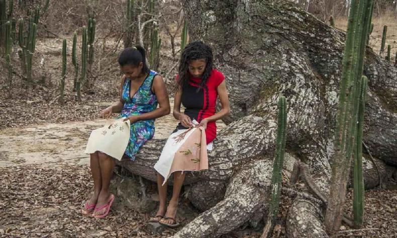 Duas mulheres bordando sentadas nas razes de uma rvore no serto de Minas Gerais