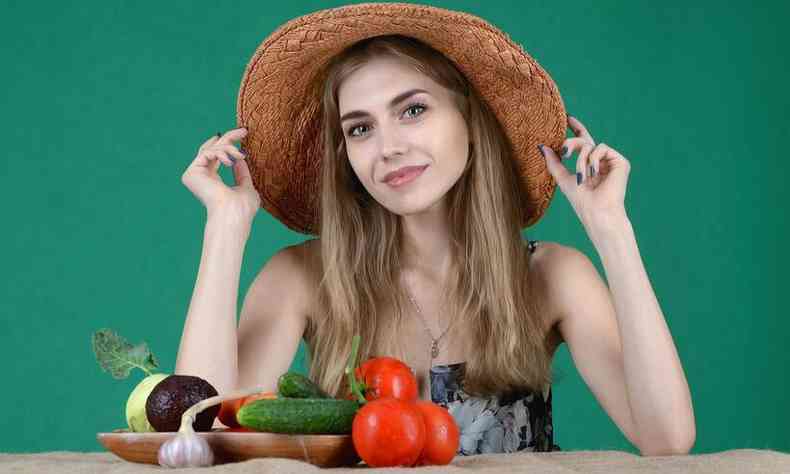 Mulher sentada em frente a uma mesa de verduras e legumes