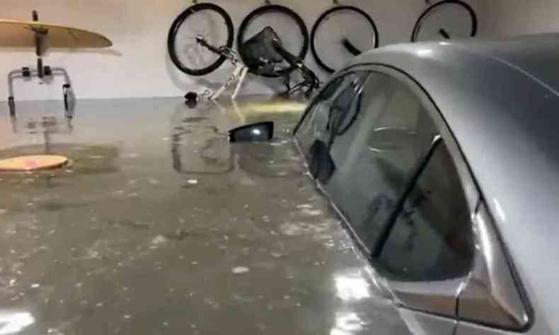 Carro inundado em uma garagem de condomnio. Imagem mostra a gua atingindo altura do vidro do veculo
