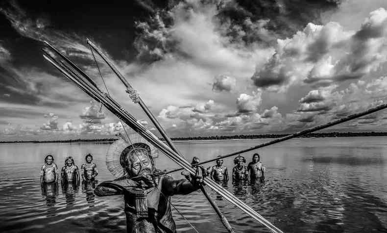 Cacique Raoni fotografado com arco e flecha, dentro do rio, por Ricardo Stuckert. Ao fundo, estão vários indígenas