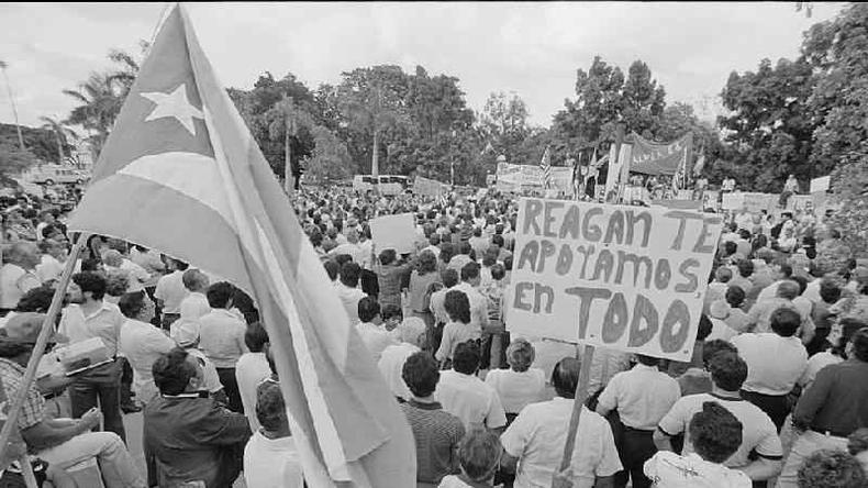 A bandeira cubana ao lado de um cartaz que diz, em espanhol, 'Reagan, te apoiamos em tudo' durante uma manifestao em 1983