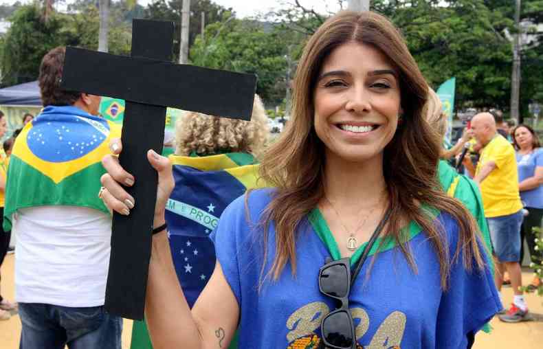 Camila leite com uma blusa azul, do brasil, sorrindo e segurando a cruz para cima