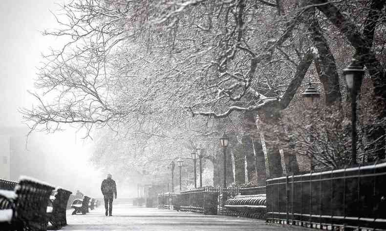 Com roupas de frio e capuz, homem caminha sob a neve no Brooklyn, em Nova York 