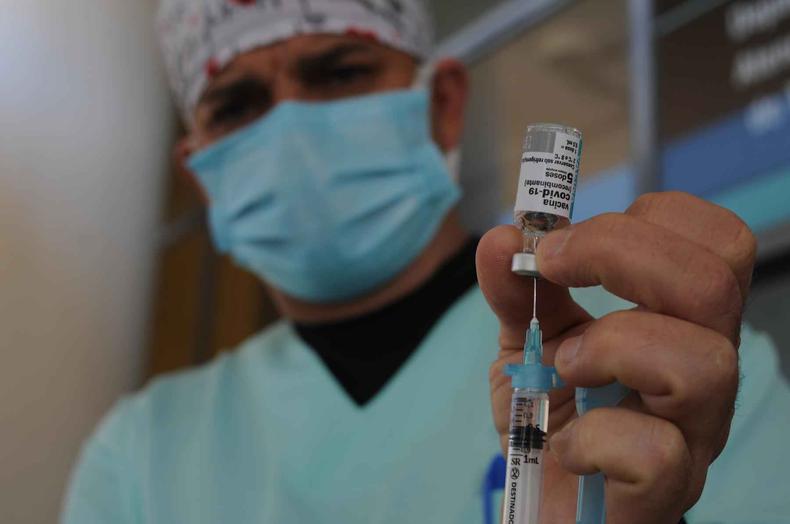 Enfermeiro prepara vacina na seringa e mostra o frasco