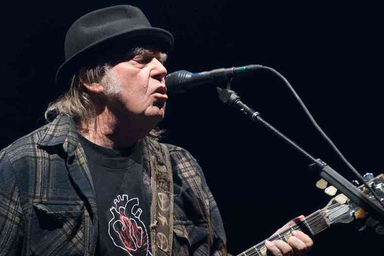 de camisa de manga comprida e tocando guitarra, Neil Young canta no palco