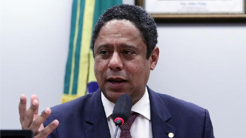 Retrato do deputado federal Orlando Silva (PC do B-SP) numa comisso da Cmara dos Deputados. Ele  um homem negro. Veste camisa social branca e gravata vinho com um terno azul marinho.