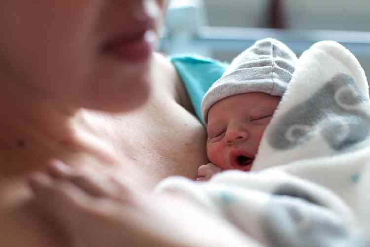Mulher com beb recm-nascido no colo em cama de hospital aps o parto