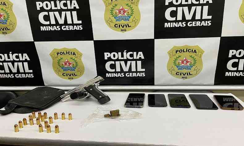 Celulares e uma pistola encontrados na casa de suspeito e expostos em mesa com logo da PCMG 