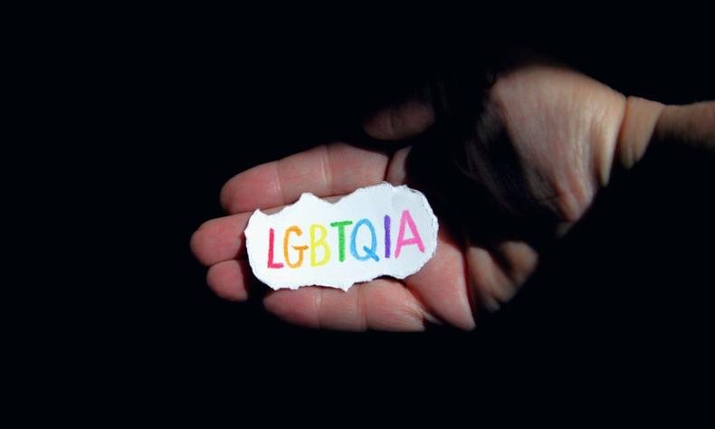M�o segurando um peda�o de papel onde esta escrito em letras mai�sculas e coloridas 'LGBTQIA'