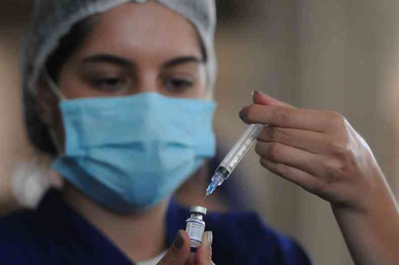 Agente de sade de mscara azul clara insere seringa em frasco contendo a vacina contra a COVID-19. 