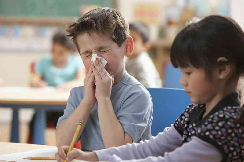 Um menino assoando o nariz na sala de aula