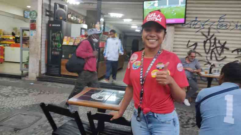 Garonete com blusa vermelha e bon do Lula sorri e faz sinal de joia com as mos