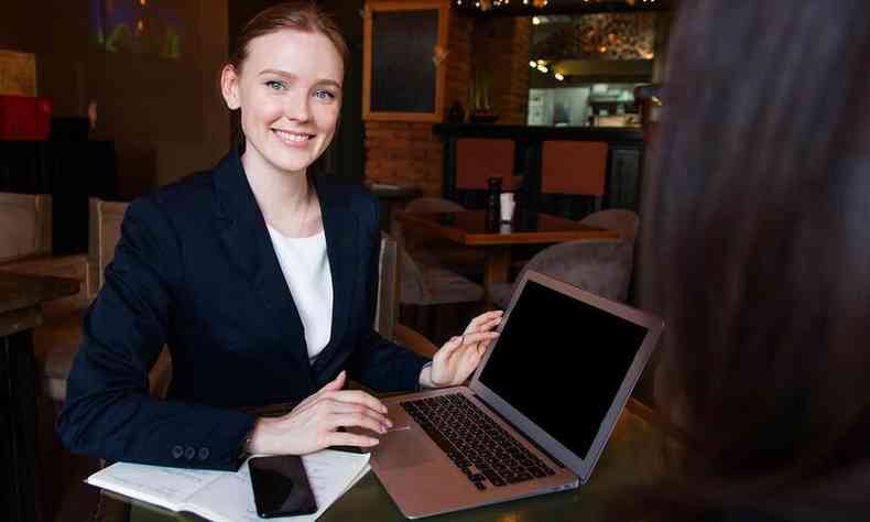 Mulher na mesa de trabalho diante de um notebook