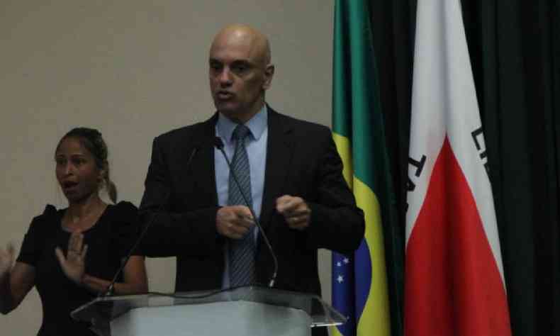 Alexandre de Moraes falando em plpito com bandeira do Brasil e de Minas Gerais ao fundo 