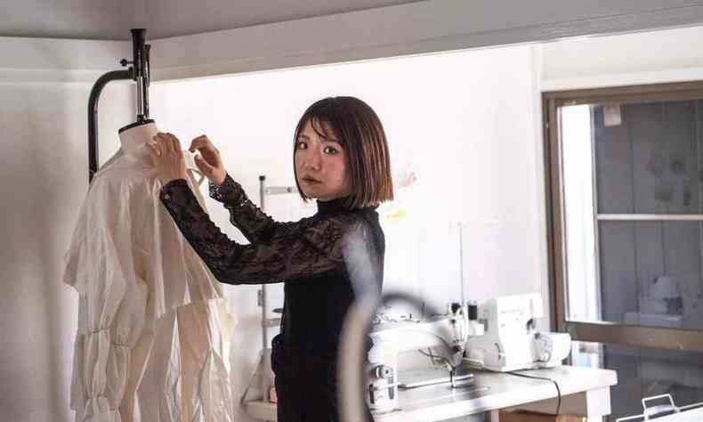 A estilista Aya Takeshima olha para a cmera e mexe em roupa pendurada em arara, num ateli de moda