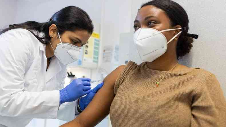 Mulher de máscara sendo vacinada