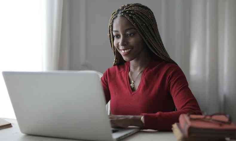 Mulher negra com cabelos tranados sorrindo enquanto utiliza o laptop