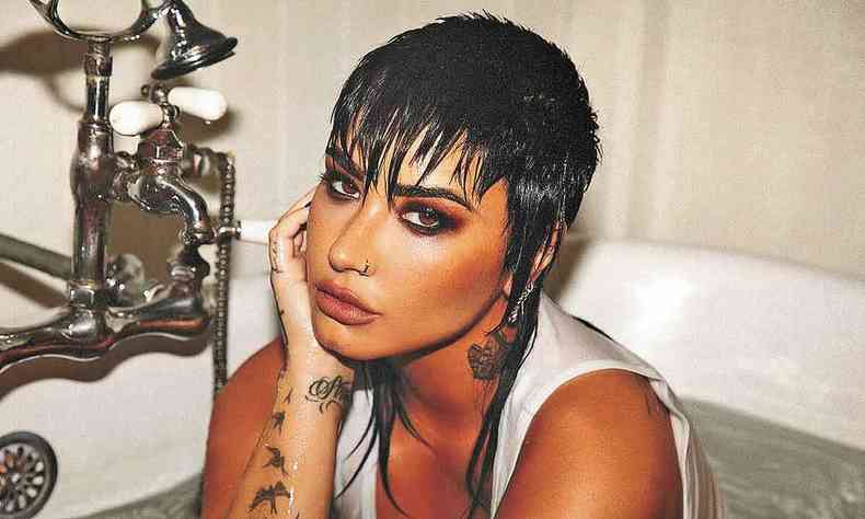 Demi Lovato, de cabelos curtos e molhados, dentro de uma banheira ao lado da torneira