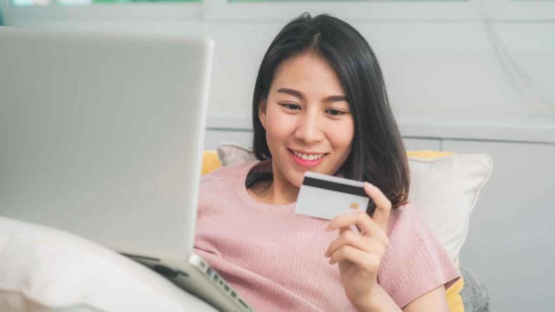 Mulher oriental deitada com notebook no colo e carto de crdito na mo esquerda