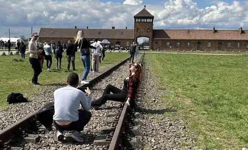 Mulher deita em linha de trem para foto em Museu Estadual de Auschwitz-Birkenau 