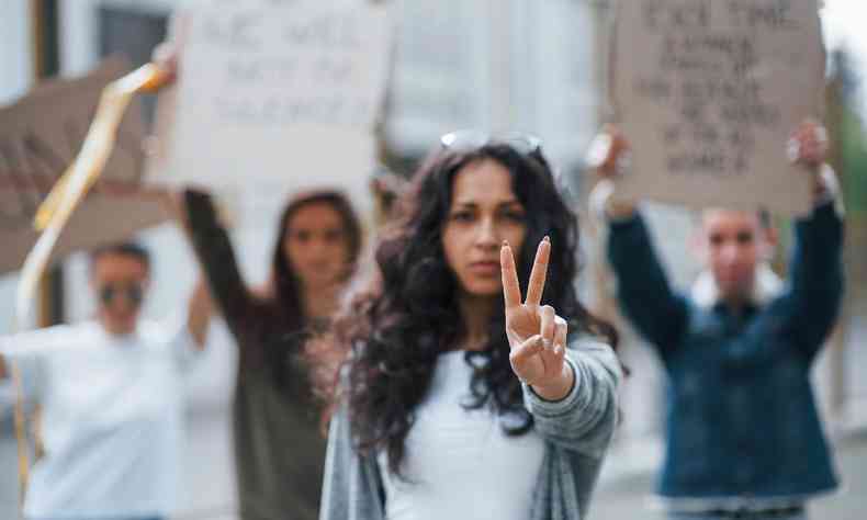 mulher em protesto levanta os dedos em V num sinal de paz