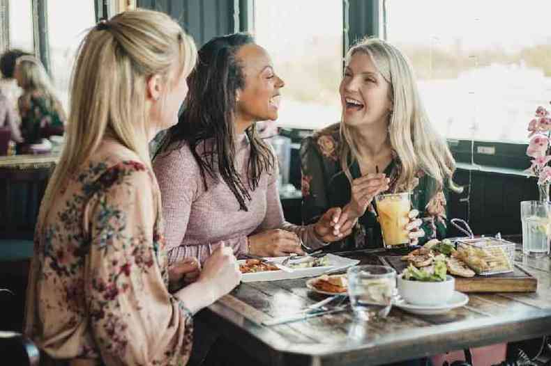 Três amigas rindo em restaurante