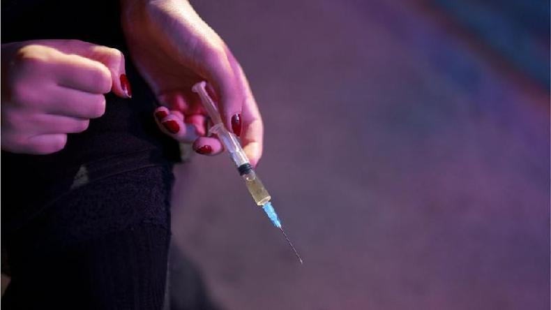 Mo de mulher branca com unhas vermelhas segura uma seringa com um lquido amarelado dentro