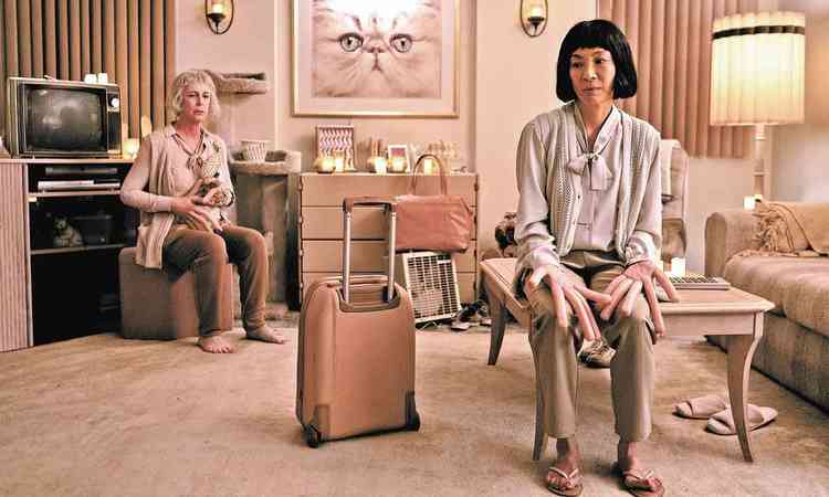 As atrizes Jamie Lee Curtis e Michelle Yeoh sentadas em sala com dedos de salsicha em cena de 'Tudo em todo lugar ao mesmo tempo'