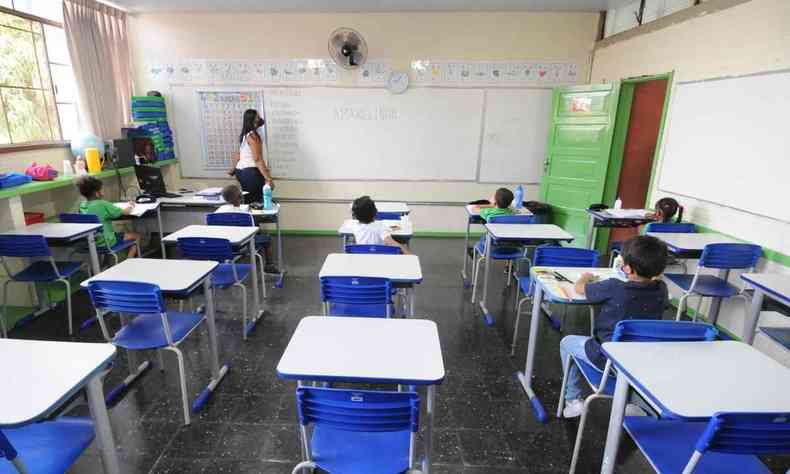 Alunos e professora em sala de aula da Escola Municipal Dom Jaime, em Belo Horizonte; carteiras de tampo branco, com cadeiras azuis