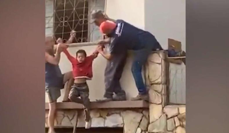 No vídeo, é possível ver que três homens fazem o resgate com ajuda de uma escada(foto: Redes sociais/Reprodução) Dois homens seguram o menino pelo braço, com ajuda de um terceiro, após já ter sido retirado da casa.
