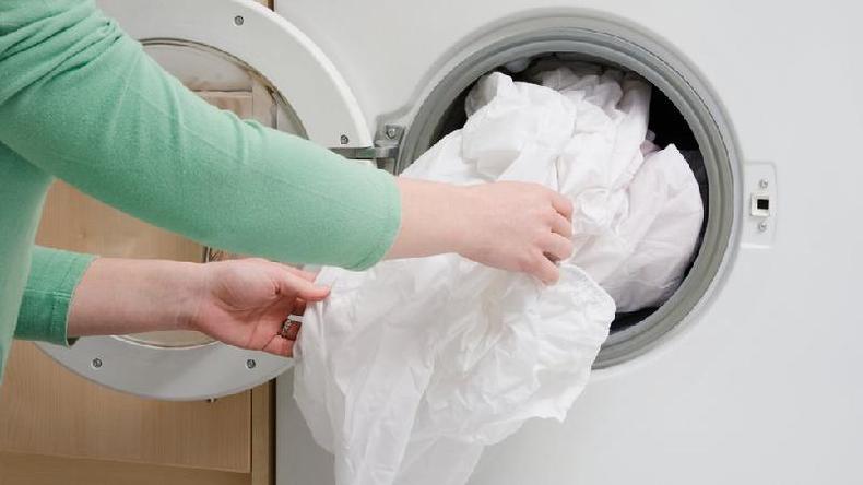 Lave a roupa de cama toda semana de acordo com as instruções do fabricante(foto: Getty Images) As mãos de uma mulher enchendo a máquina de lavar com roupa de cama