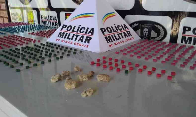 drogas dispostas em cima de uma mesa ao lado do smbolo da Polcia Militar