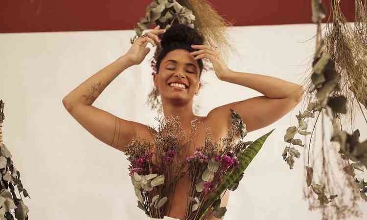 Cantora Mara Baldaia sorri, com as mos na cabea, tendo flores secas no corpo e penduradas a seu lado