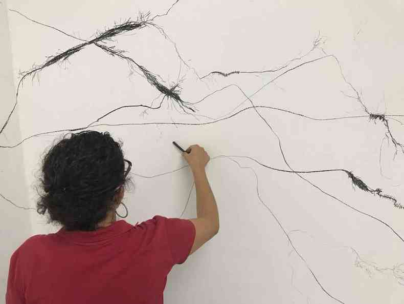 Artista plstica Camila Moreira faz desenho,usando carvo, em tela na parede