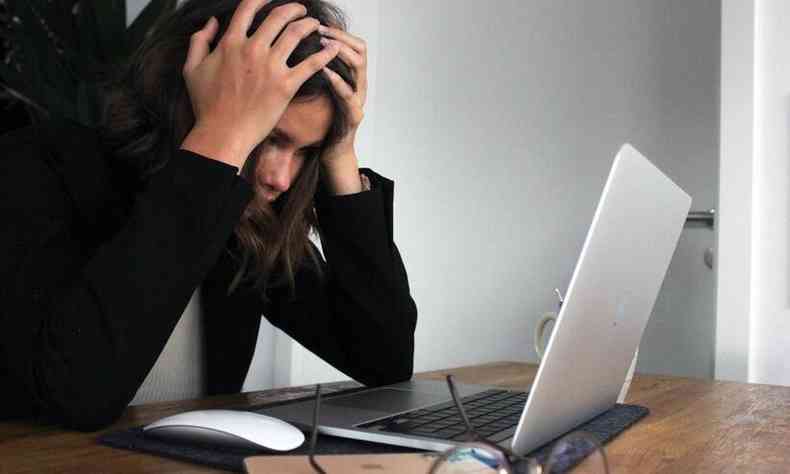 mulher na mesa de trabalho com a mo na cabea, sinal de cansao