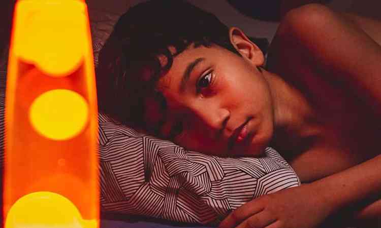 O ator mirim Matheus Brito est deitado na cama e olha para abajur laranja no curta Sideral