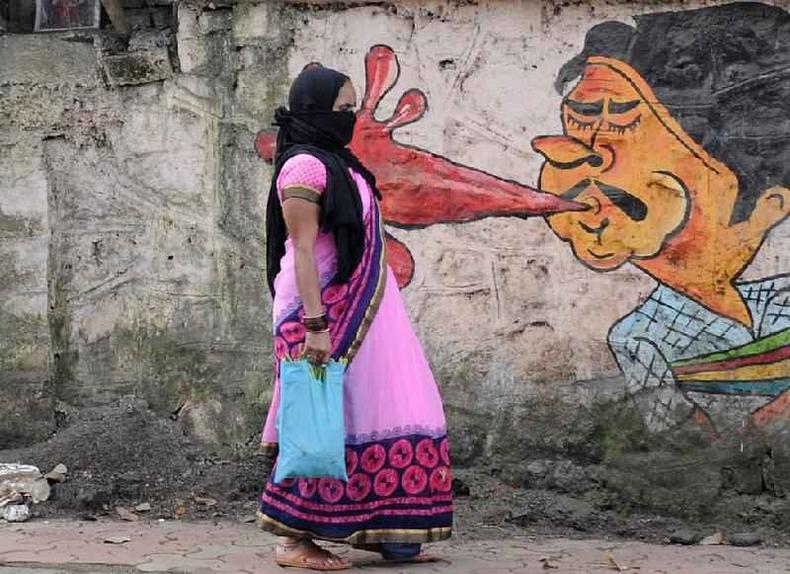 Uma mulher passa por um grafite em Mumbai, com o desenho de um homem cuspindo