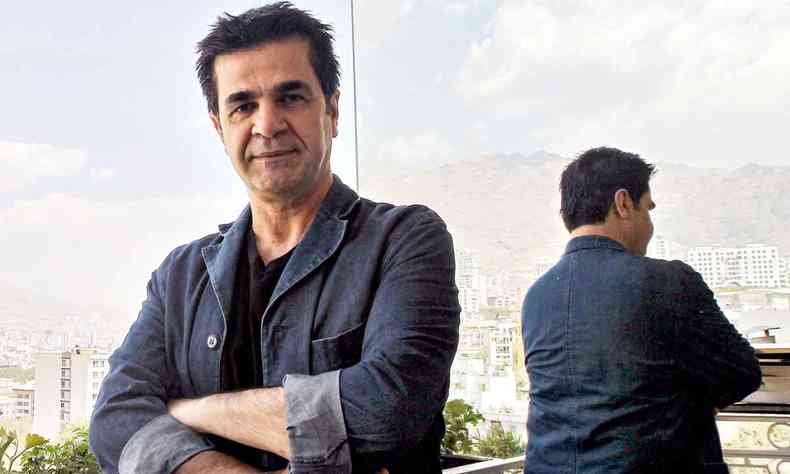 vestindo camisa jeans, em balco com Teer ao fundo, Jafar Panahi cruza os braos e olha para a cmera