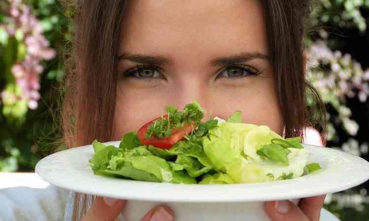 mulher com prato de salada em frente ao rosto