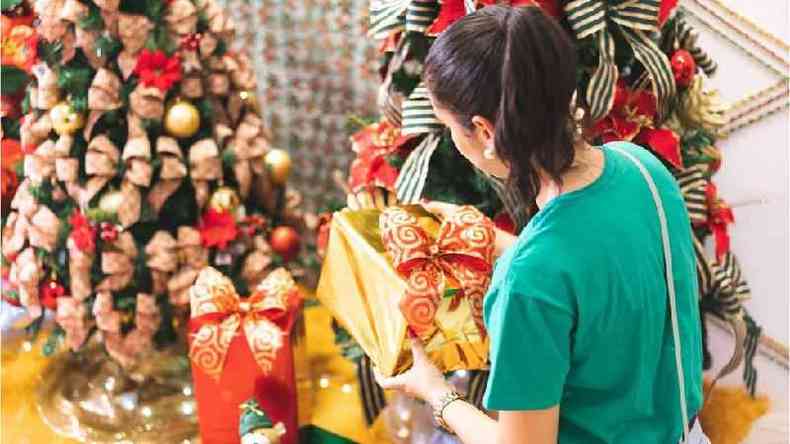 Mulher pegando presente de Natal em frente de decoraes temticas