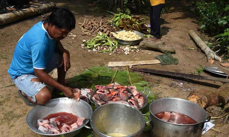 Indgena tikuna em frente a panelas com carne de animais que ser preparada para o almoo
