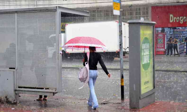 Mulher na rua com um guarda-chuva rosa, prximo a uma parada de nibus
