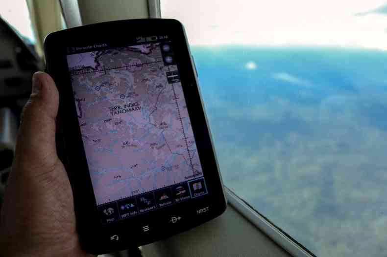 Mão segura GPS em avião enquanto sobrevoa terra yanomami