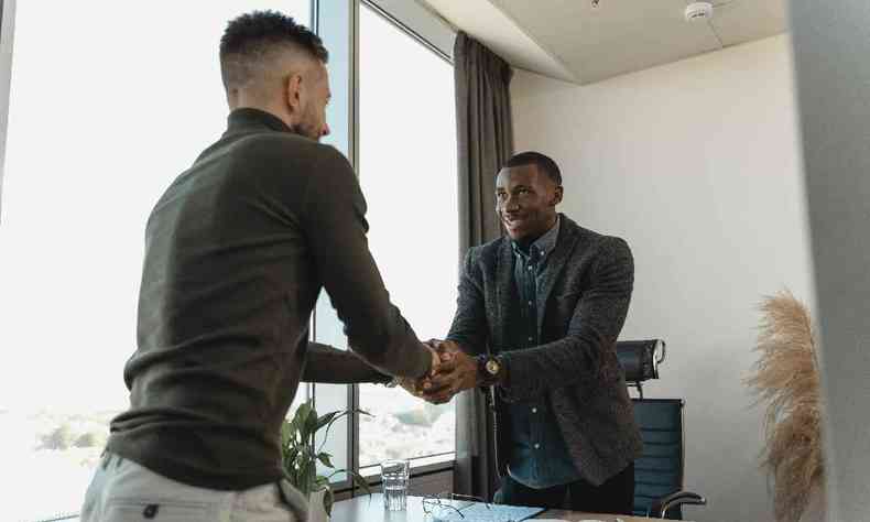 Homem negro apertando a mo de um homem branco em uma sala de reunies