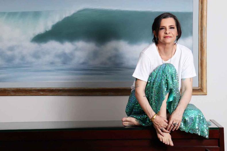 Cantora traz o show 'Nas ondas de Marina' à capital mineira(foto: Sérgio Santoian/Divulgação) Marina Lima sorri, sentada em um móvel, tendo ao fundo um quadro em tons de azul