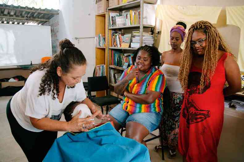 Trs mulheres negras observam outra mulher fazer limpeza de pele em cliente com o rosto coberto de gaze